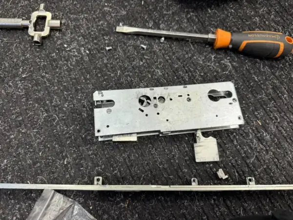 Multipoint lock gearbox removed from a uPVC door, with screwdriver and lock parts